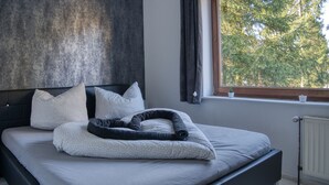 A modern bedroom with a bed, pillows, a blanket, a window with curtains, and a radiator.
