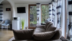 A living room with a sofa, a television, a small refrigerator, a chair, and a sliding glass door leading to an outdoor area.