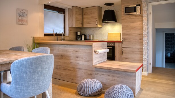 A modern kitchen with wooden cabinetry, a built-in microwave, and a dining area with a wooden table and chairs.