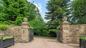 Un camino de grava conduce a una entrada porticada con muros de piedra y un cartel que dice 'Hallfield Hall'.