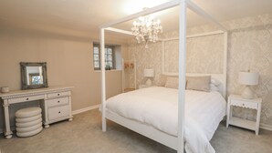 Un dormitorio con cama de dos plazas, tocador con espejo, dos mesitas de noche con lámparas y un candelabro.