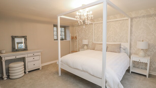 A bedroom with a four-poster bed, a vanity with a mirror, two bedside tables with lamps, and a chandelier. - Hallfield Hall Cottage (Alfreton)