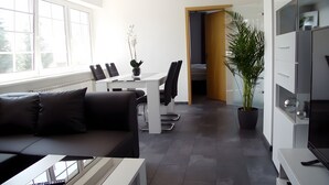 A modern living room with a sofa, a dining table with chairs, a potted plant, and a TV stand.