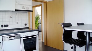 A modern kitchen with a built-in oven, a dining table with chairs, and a wooden door leading to another room.