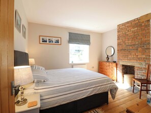 A bedroom with a bed, bedside table, lamp, dresser, mirror, and a brick fireplace. - 7 Catcliffe Cottages (Bakewell)
