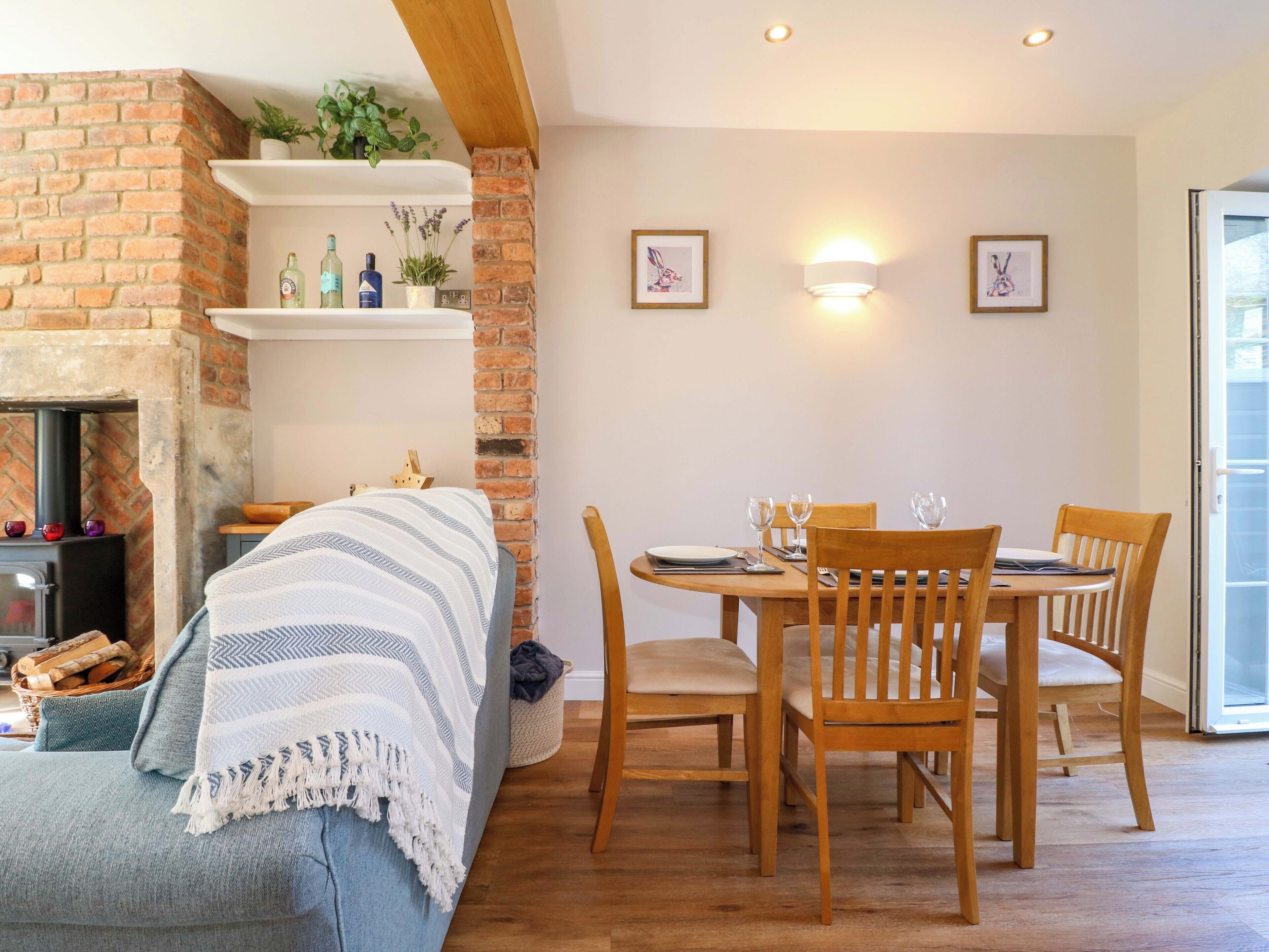 A cozy room with a brick fireplace, a dining table set for four, and two wall-mounted light fixtures.