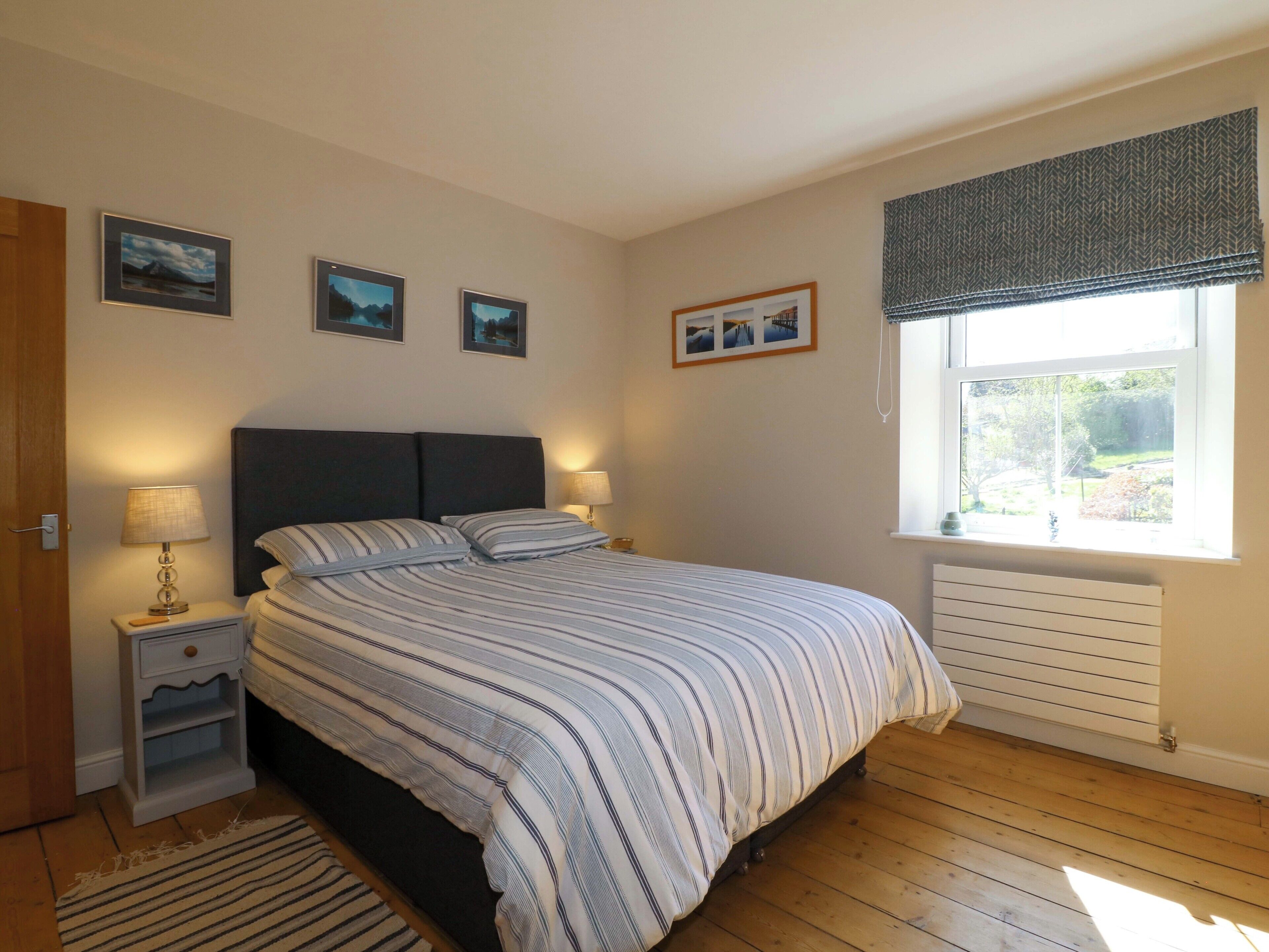 A bedroom with a bed, bedside lamps, a window with a view, and framed pictures on the wall.