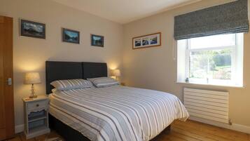 A bedroom with a bed, bedside lamps, a window with a view, and framed pictures on the wall.