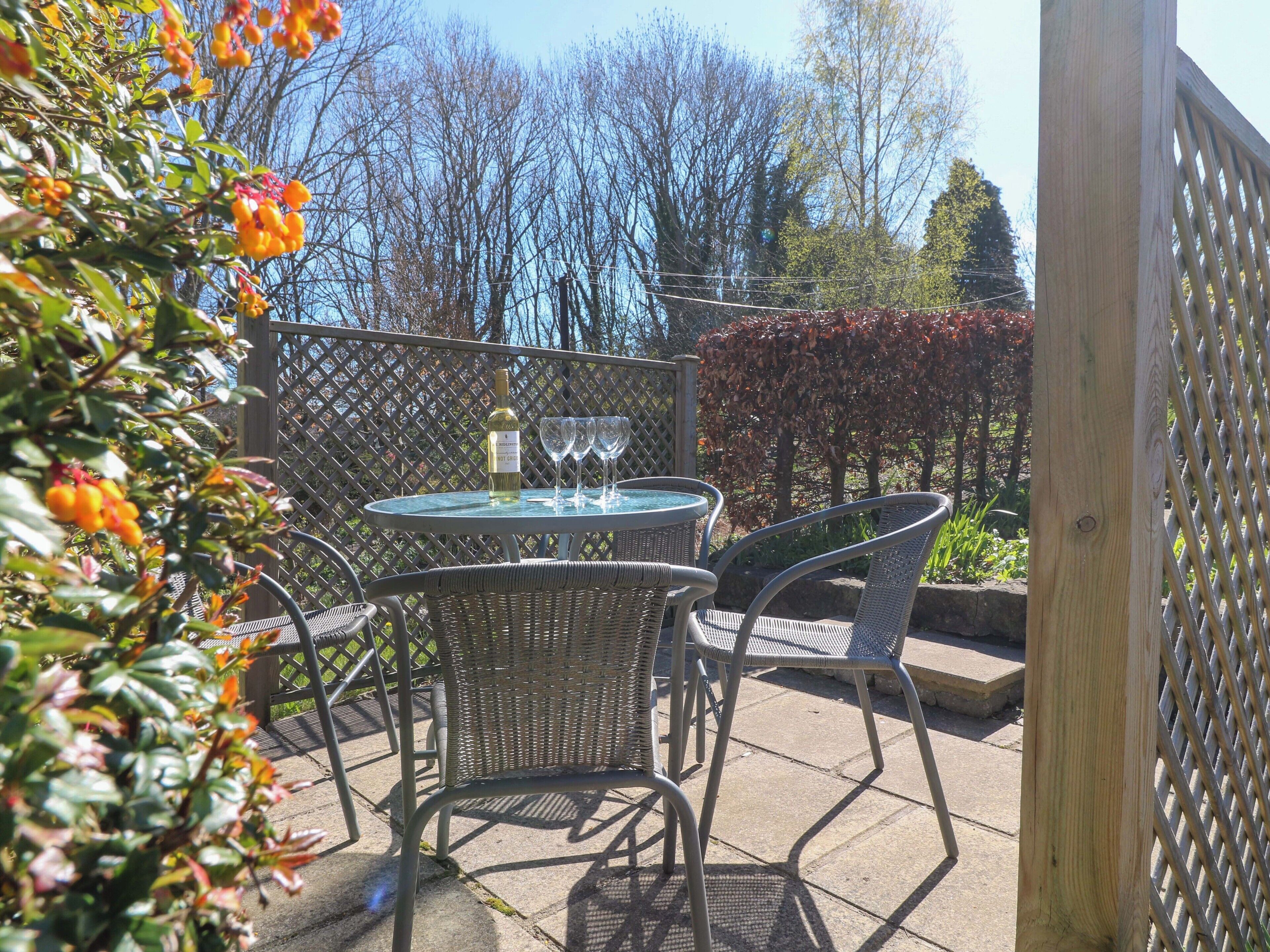 An outdoor patio with a round table, two wicker chairs, and a bottle of wine.