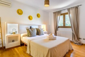 A bedroom with a bed, bedside tables, a lamp, a radiator, and a window with curtains. - Beautiful Villa Rafaella (Sant Antoni de Portmany)
