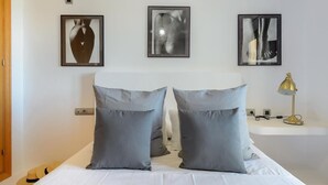 Ein Schlafzimmer mit einem Bett, zwei Kissen, einem Nachttisch mit Lampe und drei gerahmten Bildern an der Wand.