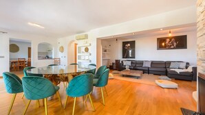 Ein modernes Wohnzimmer mit einem Esstisch mit Glasplatte, sesseln in Türkisblau, einem dunklen Sofa und einer Wand mit Steinverkleidung.