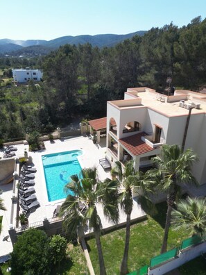 A resort with a swimming pool, palm trees, and a view of the mountains. - Beautiful Villa Rafaella (Sant Antoni de Portmany)