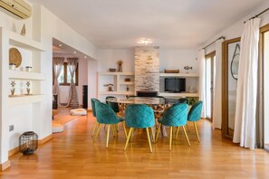 A modern living room with a dining area, wooden flooring, and teal chairs with gold legs. - Beautiful Villa Rafaella (Sant Antoni de Portmany)