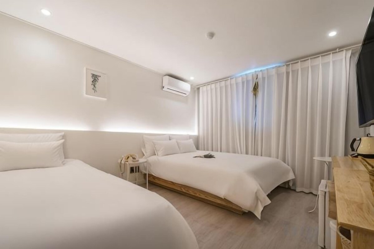 A hotel room with two beds, a desk, a chair, and a TV.