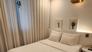 Ein Hotelzimmer mit einem großen Bett, einem Nachttisch, einer Lampe und einem Fenster mit Vorhängen.