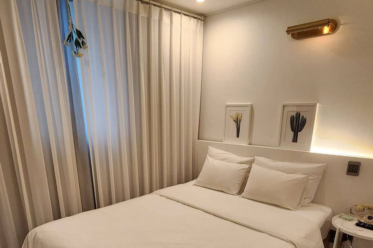 Habitació d'hotel amb un llit gran, una taula de nit, una làmpada i una finestra amb cortines.