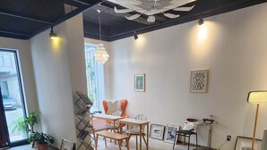 Ein geräumiges Zimmer mit hohen Decken, einem Essbereich mit Tisch und Stühlen, einer Stehlampe und gerahmten Kunstwerken an den Wänden.
