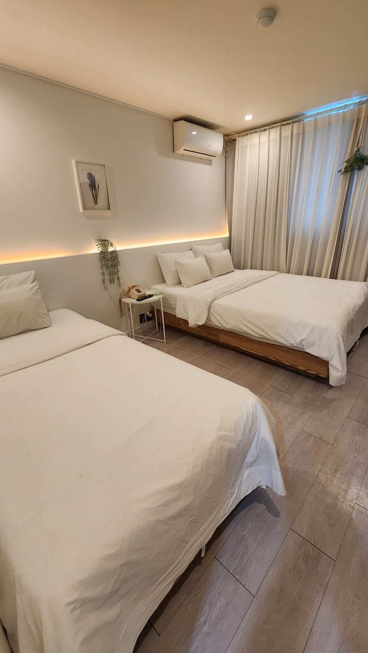 Ein Hotelzimmer mit zwei Betten, einem Nachttisch mit Telefon, einer Wand-Klimaanlage und einem Fenster mit Vorhängen.