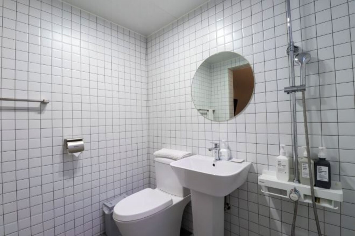 A bathroom with white tiled walls, a round mirror, a sink, a toilet, and a shower.