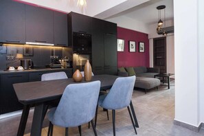 Eine moderne Küche mit dunklen Schränken, einem Esstisch mit Stühlen und einer Wohnbereits mit einer Couch und einer roten Akzentwand.