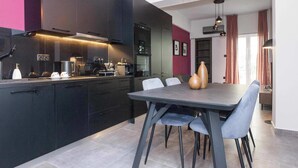 A modern kitchen with dark cabinetry, a dining table with chairs, and a vase on the table. - Premium Designer Retreat in Central Athens Gizi (Athina)