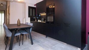 A modern kitchen with dark cabinetry, a dining table with chairs, and a pendant light fixture. - Premium Designer Retreat in Central Athens Gizi (Athina)