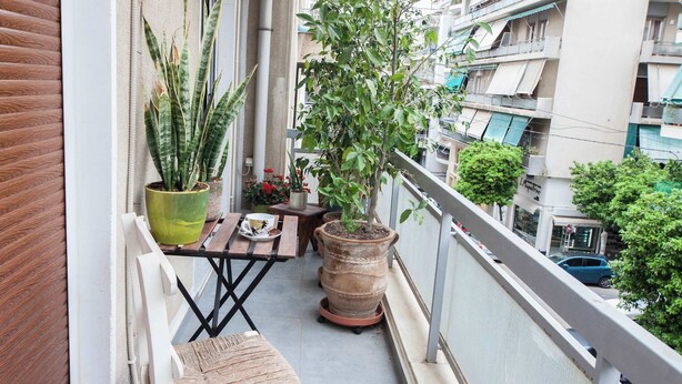 A balcony with a chair, a small table, potted plants, and a view of the city. - Premium Designer Retreat in Central Athens Gizi (Athina)