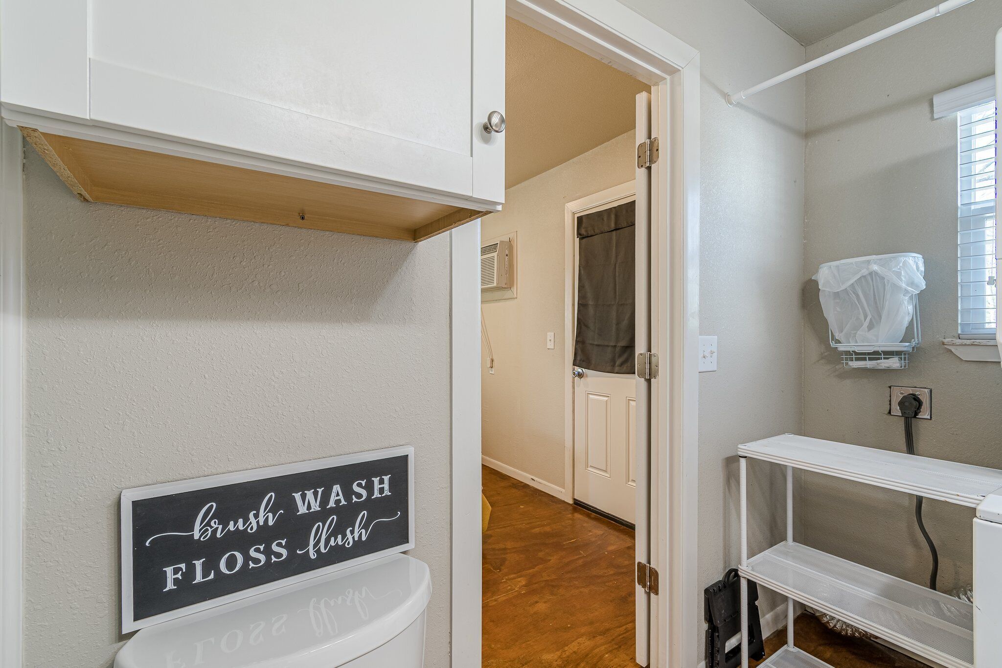 Une salle de bain avec une pancarte indiquant « Se brosser les dents, se rincer la bouche, utiliser le fil dentaire, tirer la chasse d’eau » et des toilettes blanches.