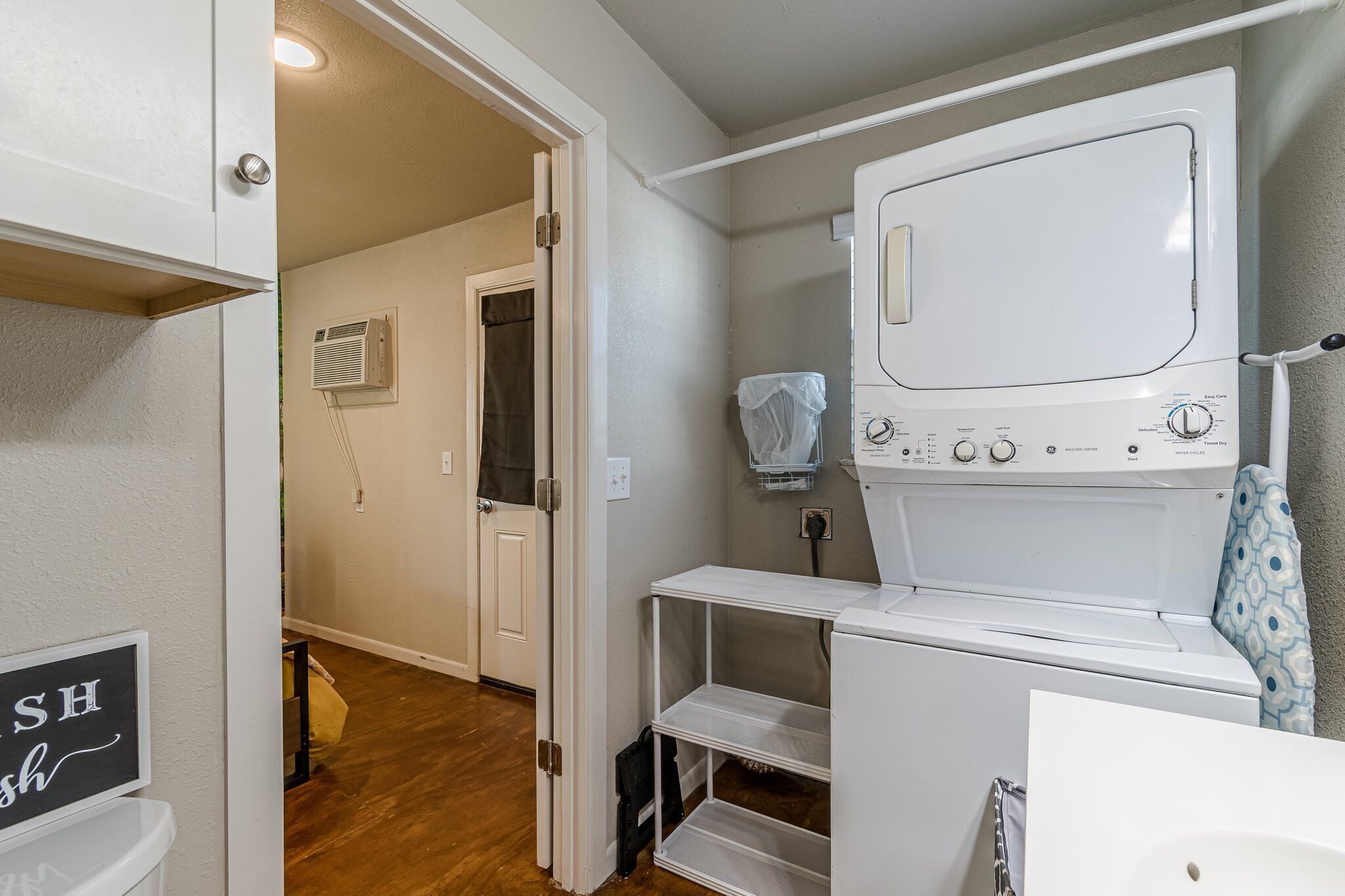 A laundry room with a front-loading washer and dryer, a shelf, and a door leading to another room.