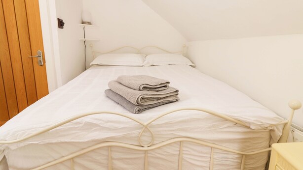 A bedroom with a bed, a wooden door, and a white wall. - Artists Cottage (Turraheen Lower)