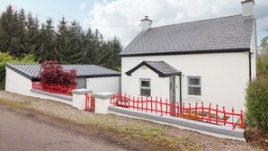 A white house with a grey roof, a red fence, and a small garden. - Artists Cottage (Turraheen Lower)