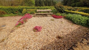 A gravel area with a wooden bench and flower beds. - Artists Cottage (Turraheen Lower)