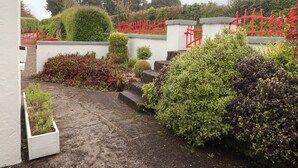 A garden with a paved path, a red gate, and various shrubs. - Artists Cottage (Turraheen Lower)