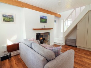 A living room with a sofa, fireplace, wooden beams, and a staircase.