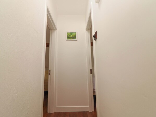 A narrow hallway with white walls, a wooden floor, and a door at the end.