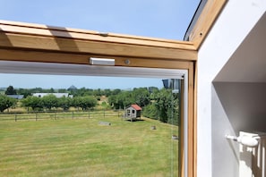 Blick durch ein Fenster mit Holzrahmen auf eine kleine Gartenhütte und einen eingezäunten Hof.