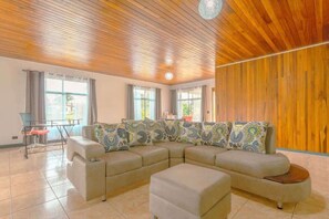 A living room with a sectional sofa, ottoman, and a dining table with chairs. - Gray Oasis, Private Pool (La Fortuna)