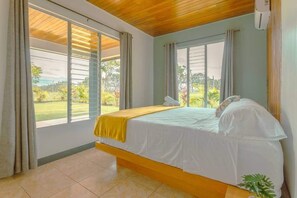 A bedroom with a bed, large windows, and a view of greenery. - Gray Oasis, Private Pool (La Fortuna)