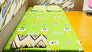 A small, single-bed room with a patterned wall, a green mattress with cartoon characters, and a patterned pillow. - Bintang Sawarna 2 By ARBA (Bayah)