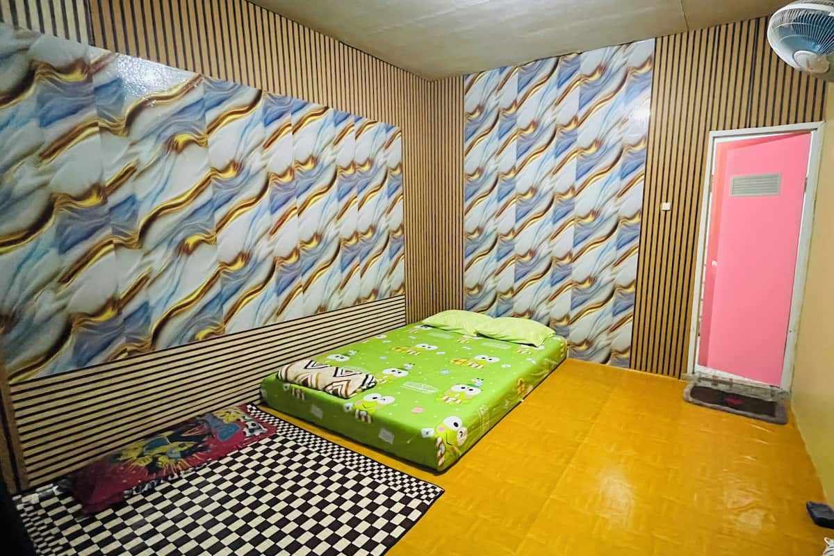 A room with a bed, a fan, a checkered rug, and patterned wallpaper.