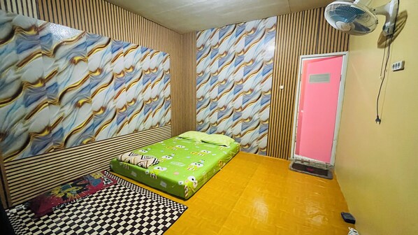 A room with a bed, a fan, a checkered rug, and patterned wallpaper.