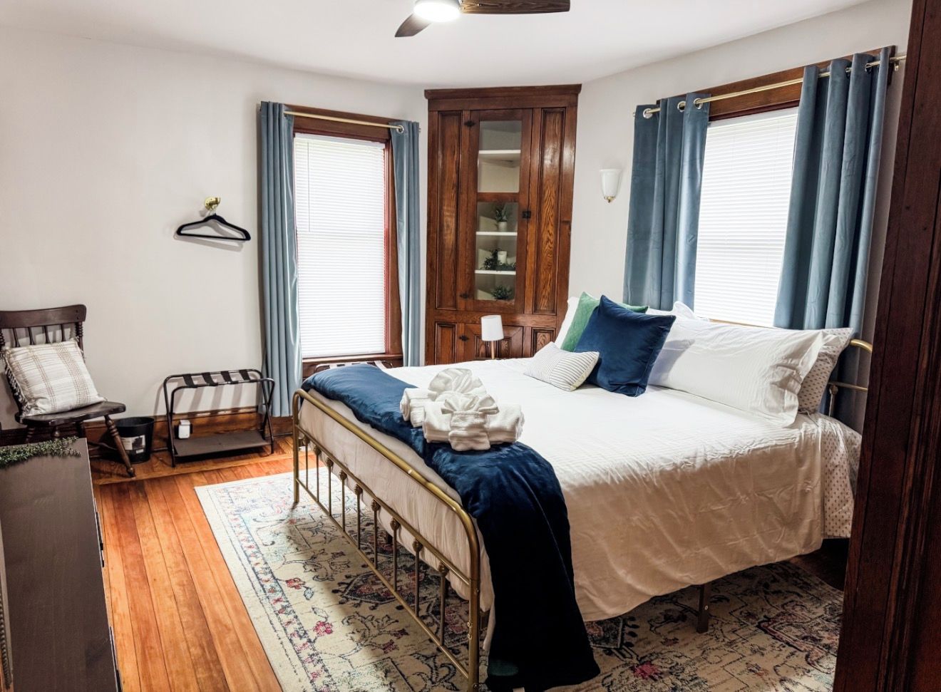 A bedroom with a bed, a wooden wardrobe, a chair, and a window with curtains.