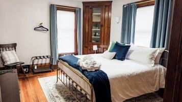 A bedroom with a bed, a wooden wardrobe, a chair, and a window with curtains.