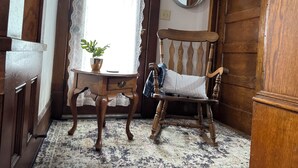 Une chaise en bois avec un coussin, une petite table avec une plante et un miroir au mur.