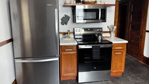 Une cuisine équipée d’un réfrigérateur en acier inoxydable, d’un four à micro-ondes, d’un four traditionnel, de meubles de rangement en bois et d’un plan de travail en marbre.