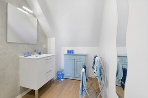 Un baño moderno con un espejo grande, tocador blanco, gabinete azul y un tendedero.