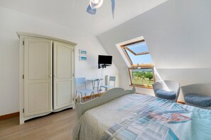 Une chambre à coucher comprenant un lit, une armoire, un téléviseur, deux chaises, une petite table et une fenêtre de toit.