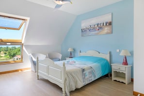 Un dormitorio con una cama, una silla, una mesita de noche, una lámpara, un cuadro y un tragaluz.