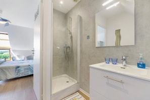 Une salle de bain moderne avec une douche à parois de verre, un lavabo blanc avec deux verres et un miroir.